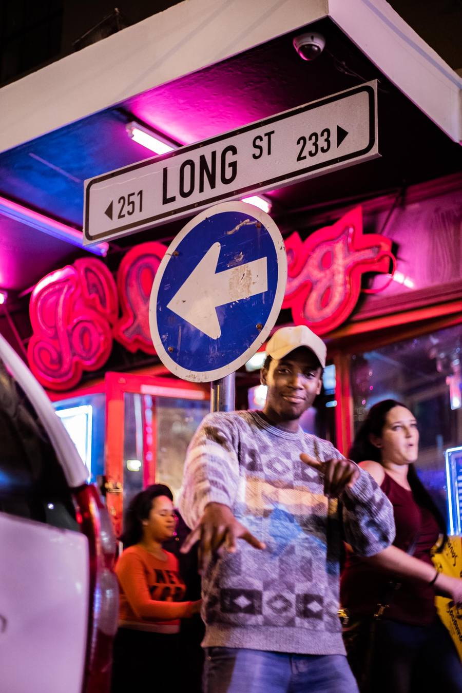 A man points at a street sign while two women walk behind him
