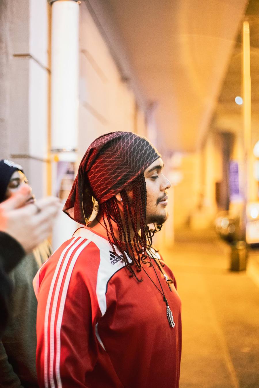 A man with dreadlocks wearing a red Adidas tracksuit and a bandana