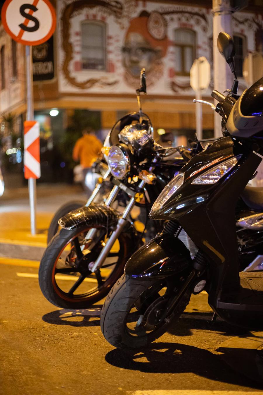 Three motorcycles parked on a street at night with a building in the background.