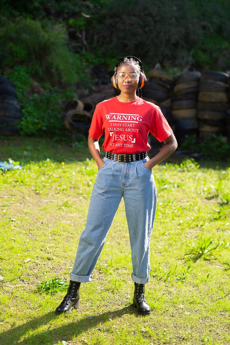 Woman in red t-shirt and jeans standing in grass with hands in pockets