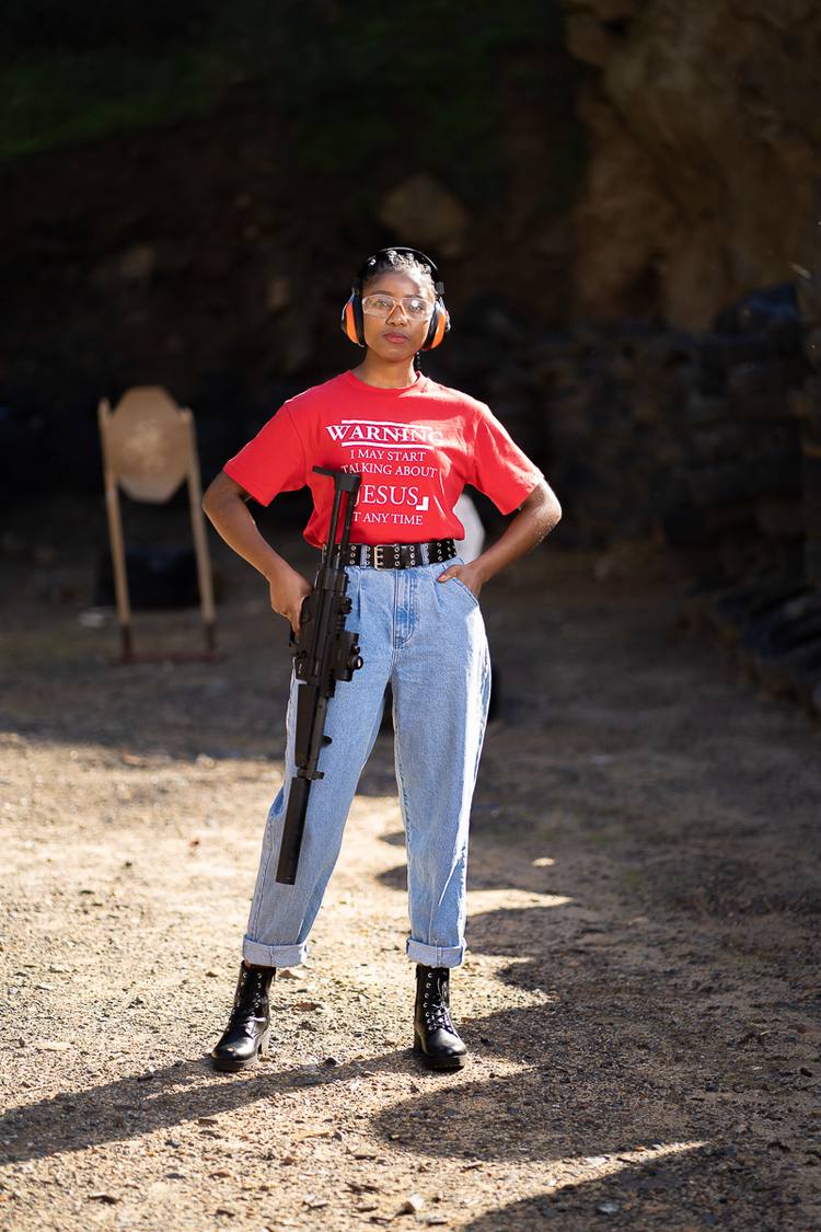 Woman in red t-shirt and jeans holding a rifle at a shooting range