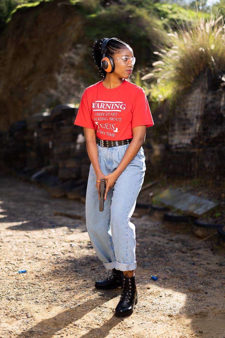 Woman in red t-shirt and jeans holding a gun at a shooting range