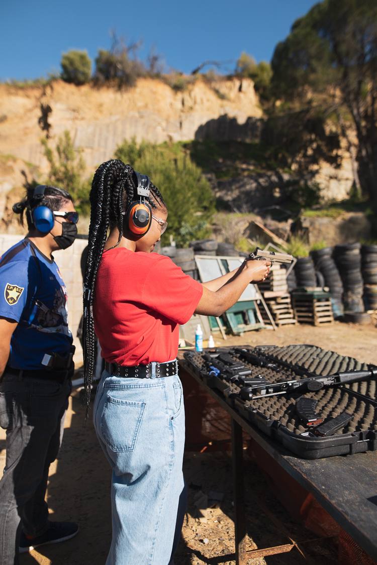 Woman in red shirt holding gun at shooting range with instructor