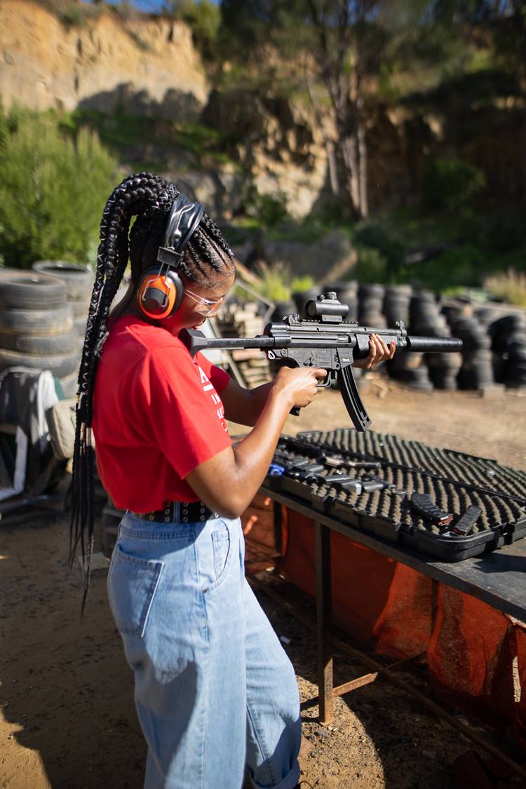Woman in red shirt and headphones holding a rifle at a shooting range.