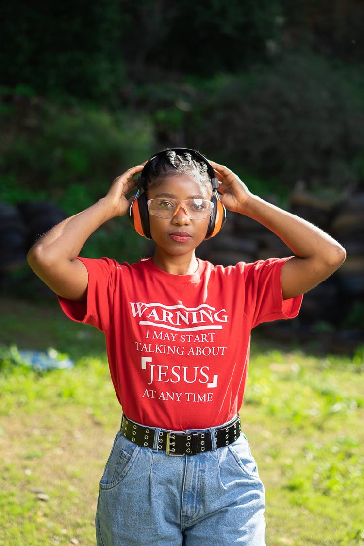 Woman wearing headphones and red t-shirt with white writing standing in a grassy area