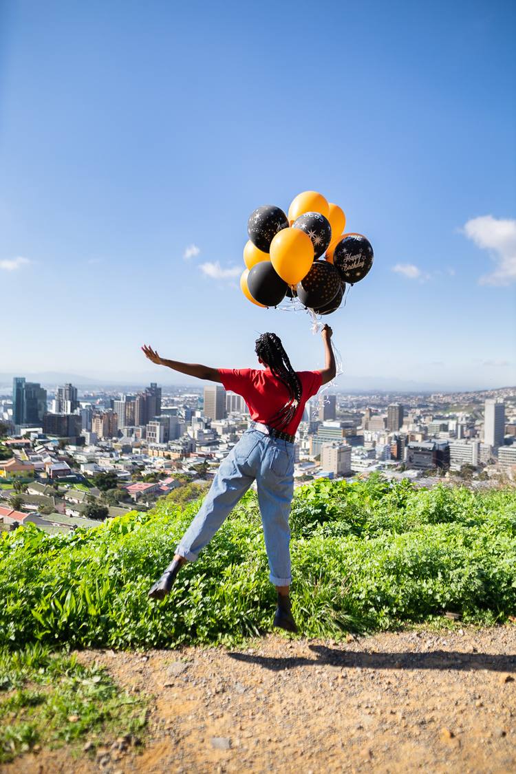 Woman jumping with arms outstretched holding a bunch of balloons over a city