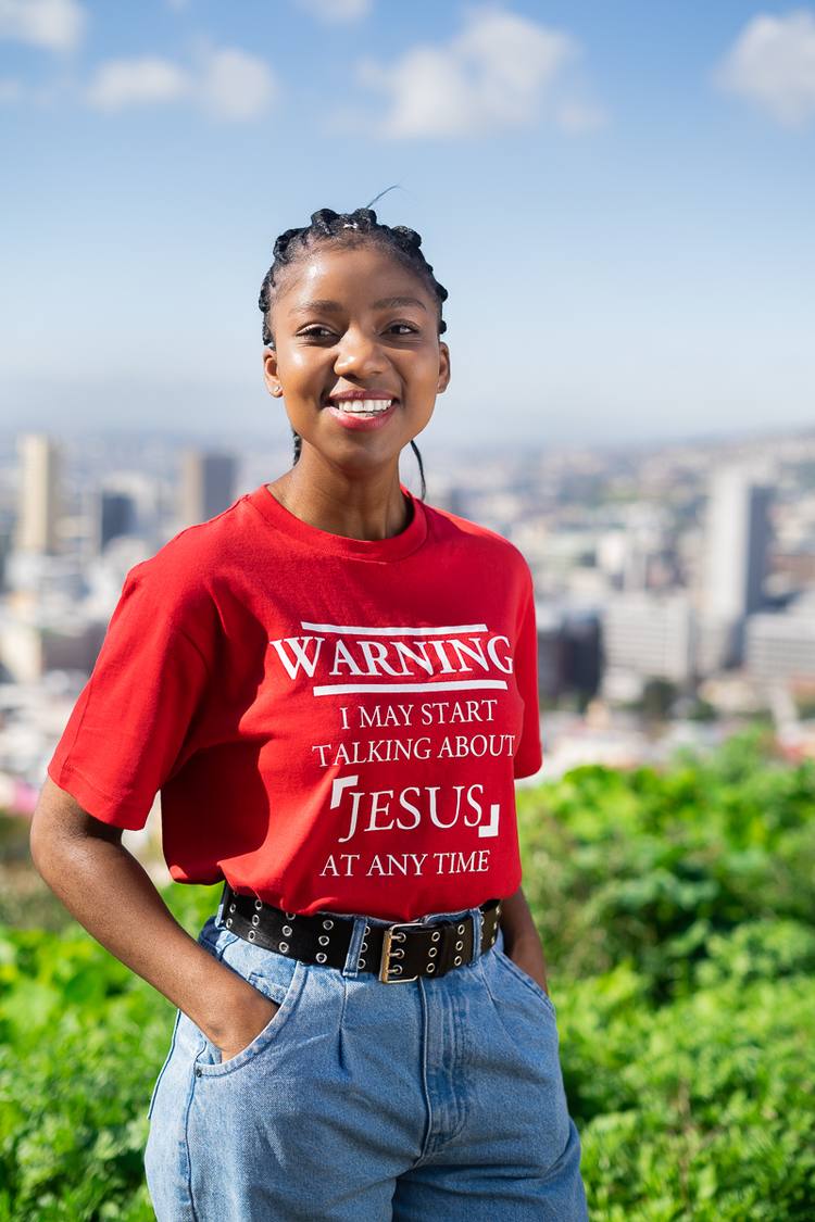 Woman in red t-shirt with Jesus print, standing with hands in pockets, smiling