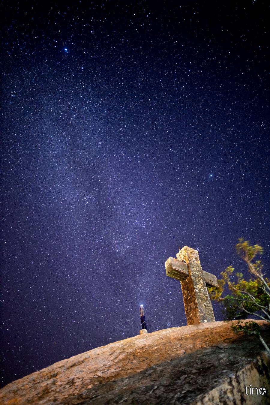 A person stands on a hilltop with a stone cross and a starry sky