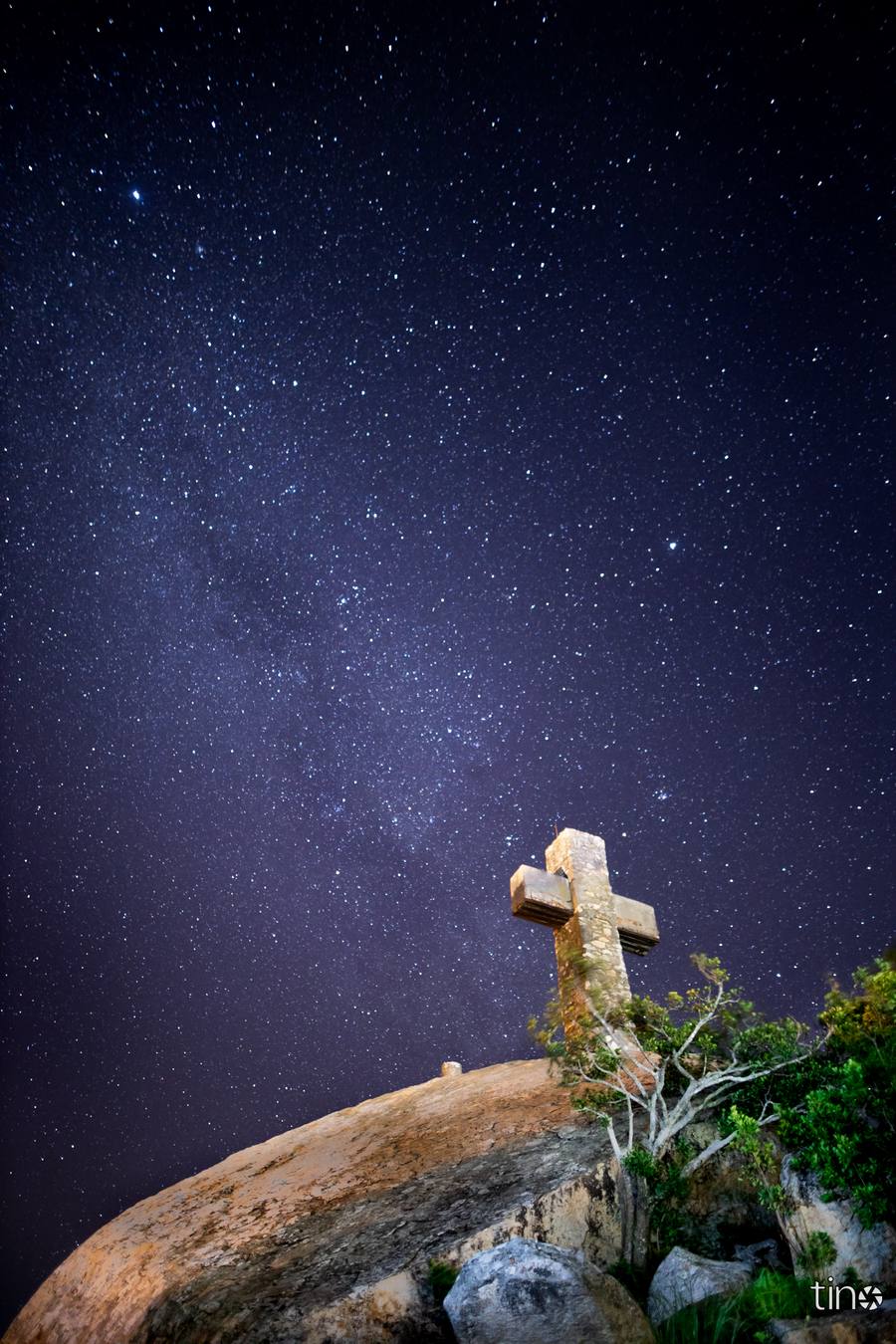 A cross on a hilltop under a star-filled night sky