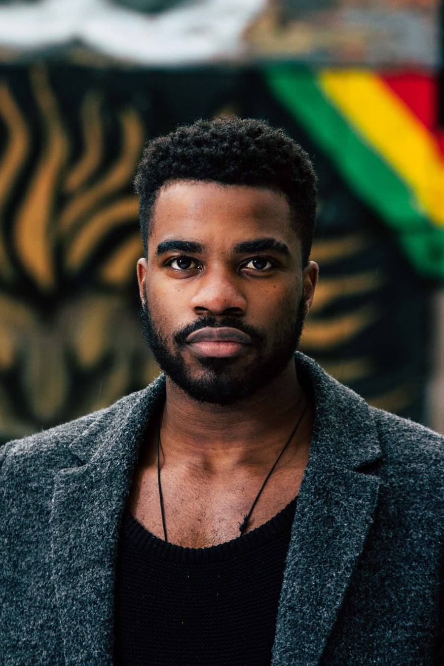 Man with beard and necklace in front of a black and yellow backdrop