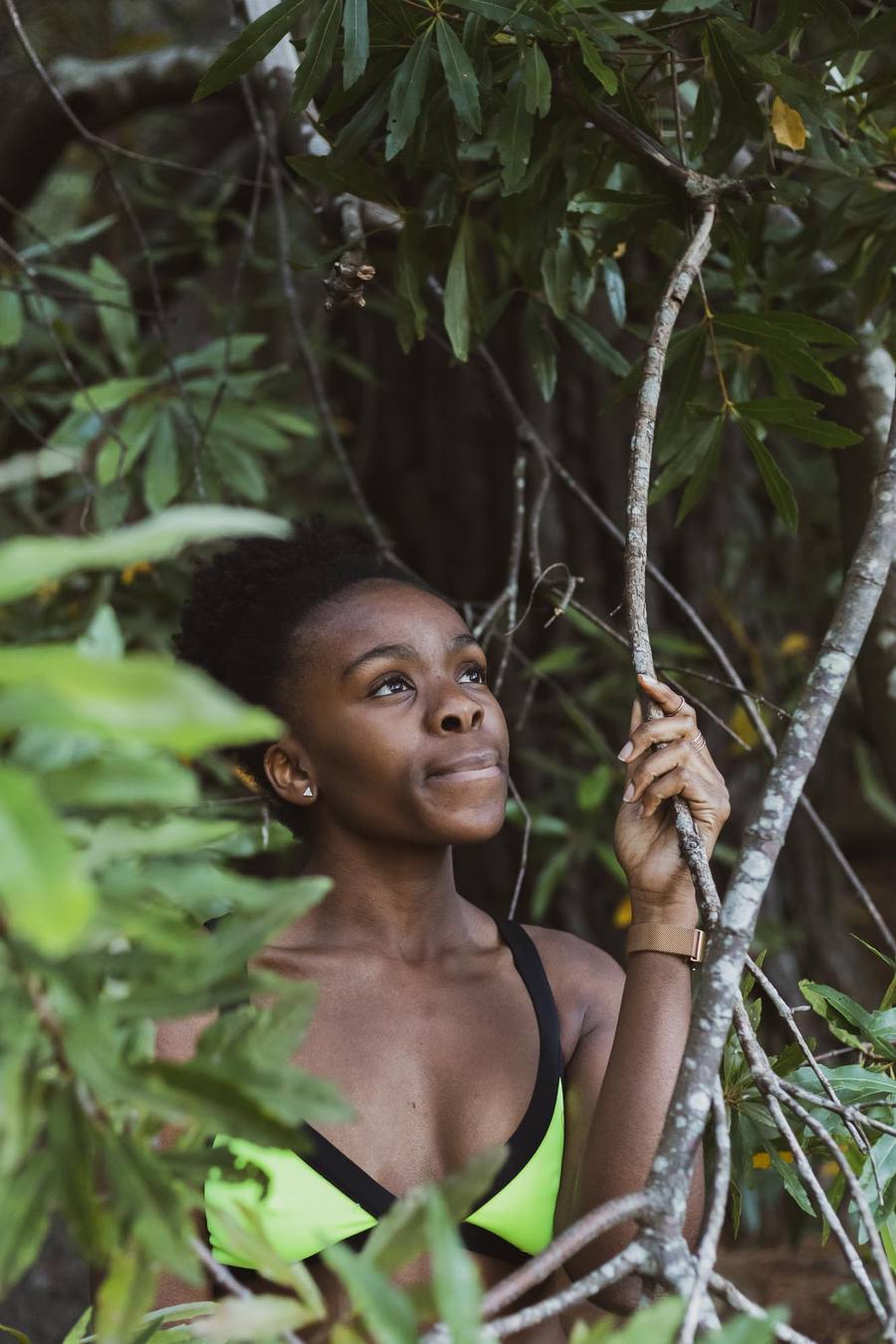 Woman in green and black bikini holding a branch in a forest