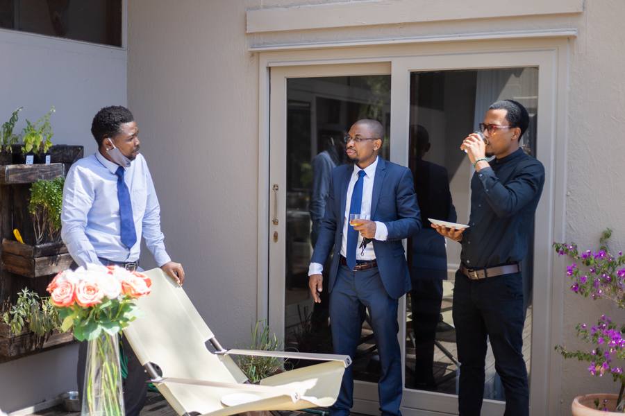 Three men in suits stand outside, one drinks from a glass, another holds a plate
