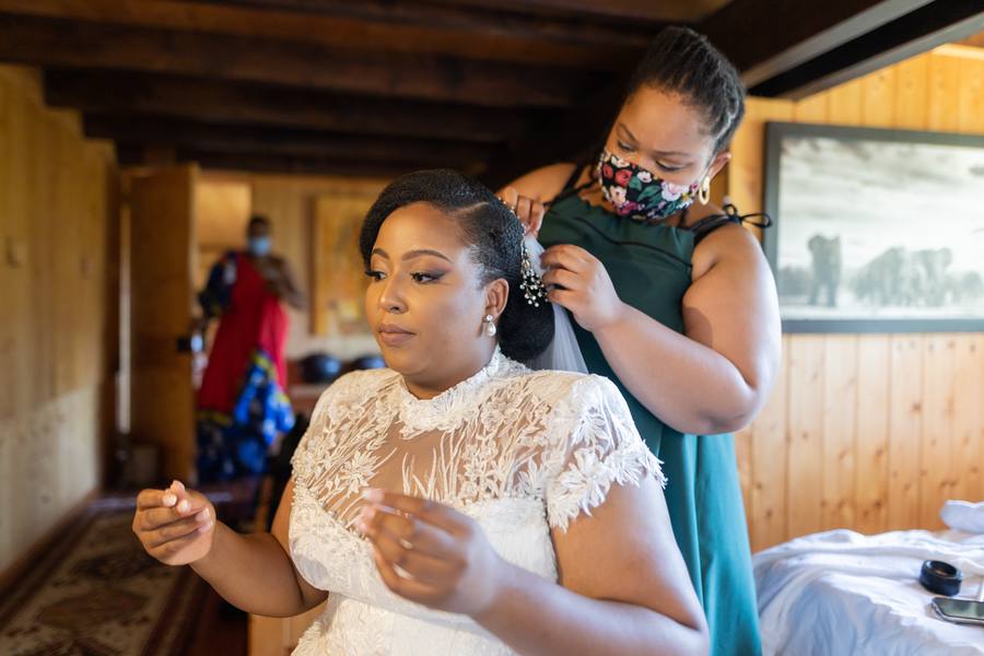 A bride in a white dress getting her hair styled by a woman in a green dress.