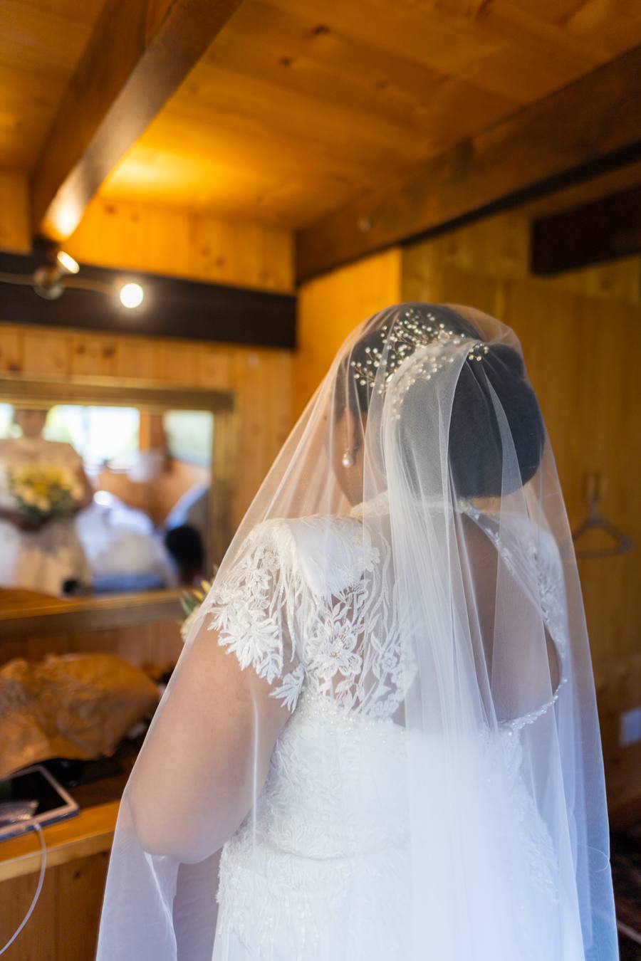 Bride in wedding dress and veil, back view, wooden room, mirror reflection