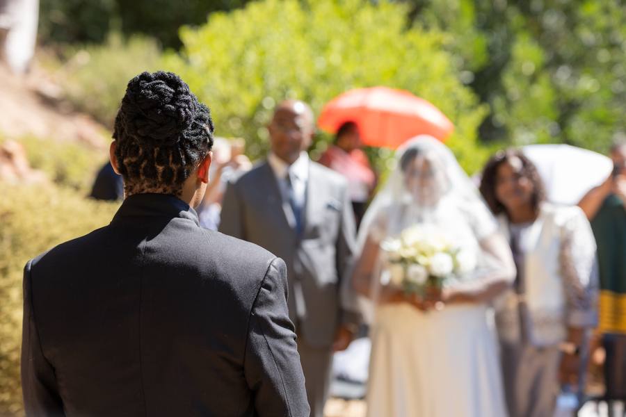 A groom watches the bride walk down the aisle with a bouquet