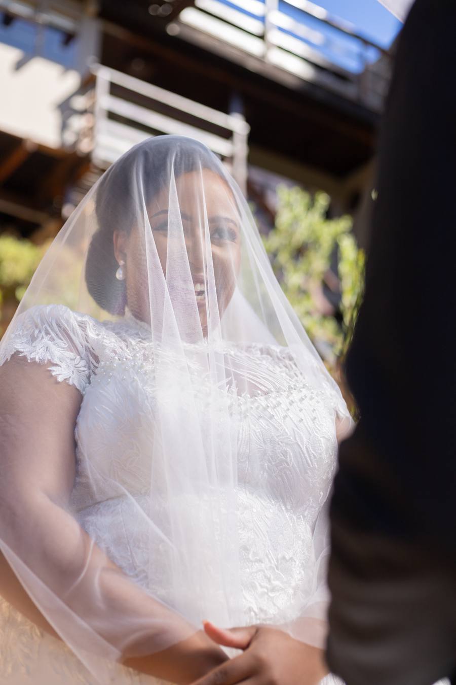 Bride in wedding dress and veil smiles at groom, holding his hands