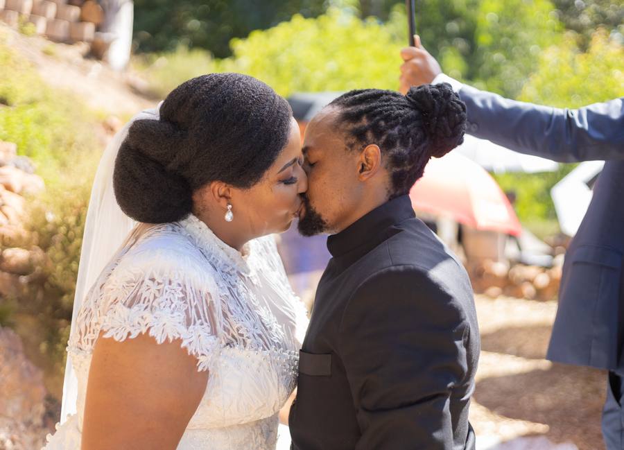 Bride and groom share a kiss with a blurred umbrella in the background.