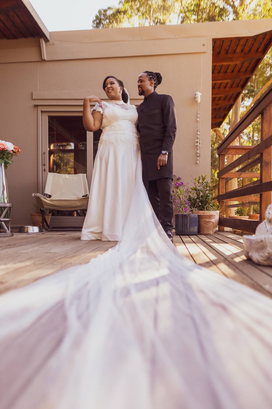 Bride and groom stand on a wooden deck with a long train of the bride's dress.