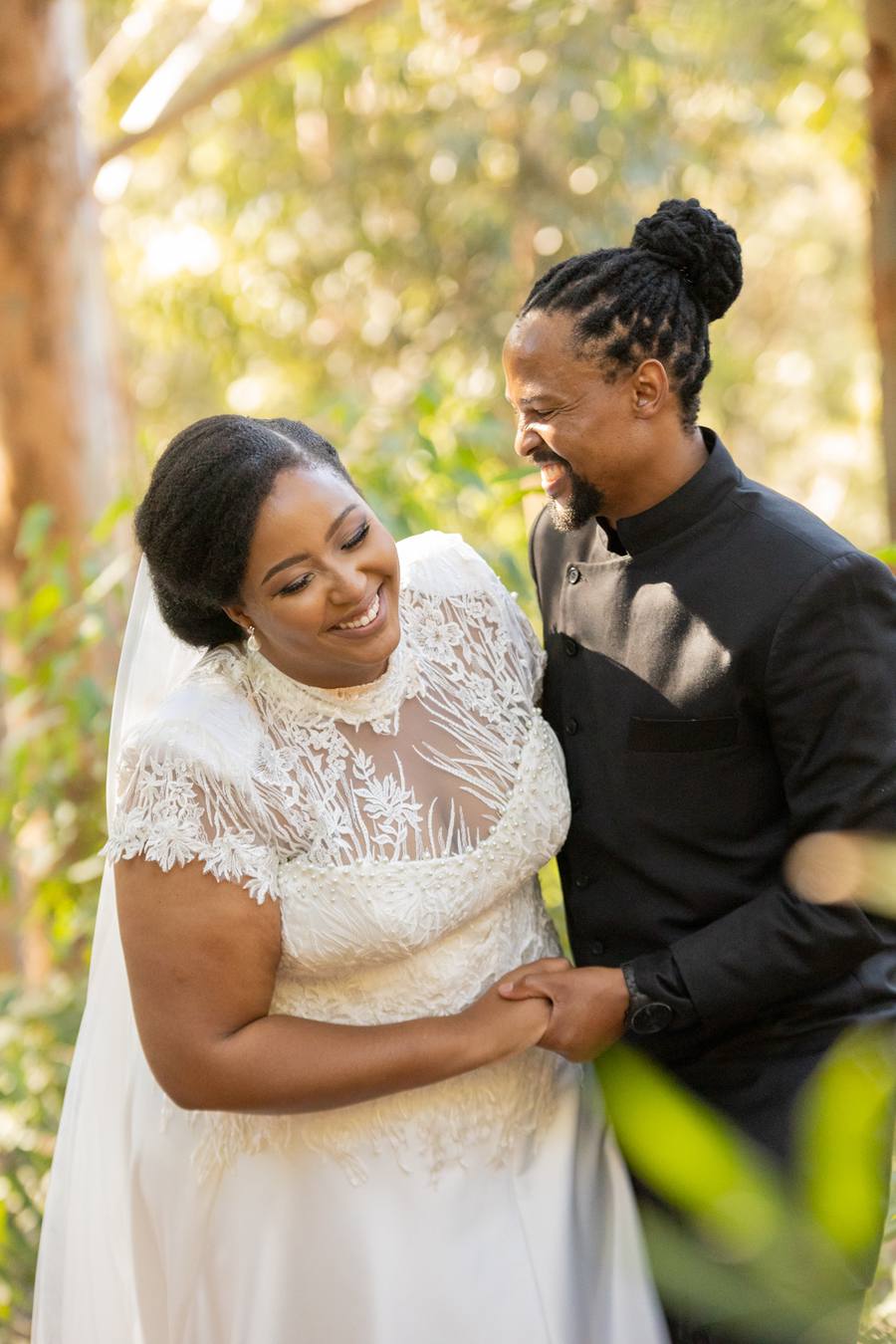 A smiling bride and groom hold hands in a forest setting