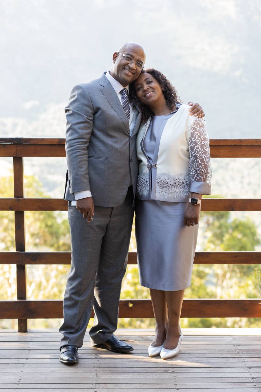 A couple stand close together on a wooden deck, smiling at the camera.