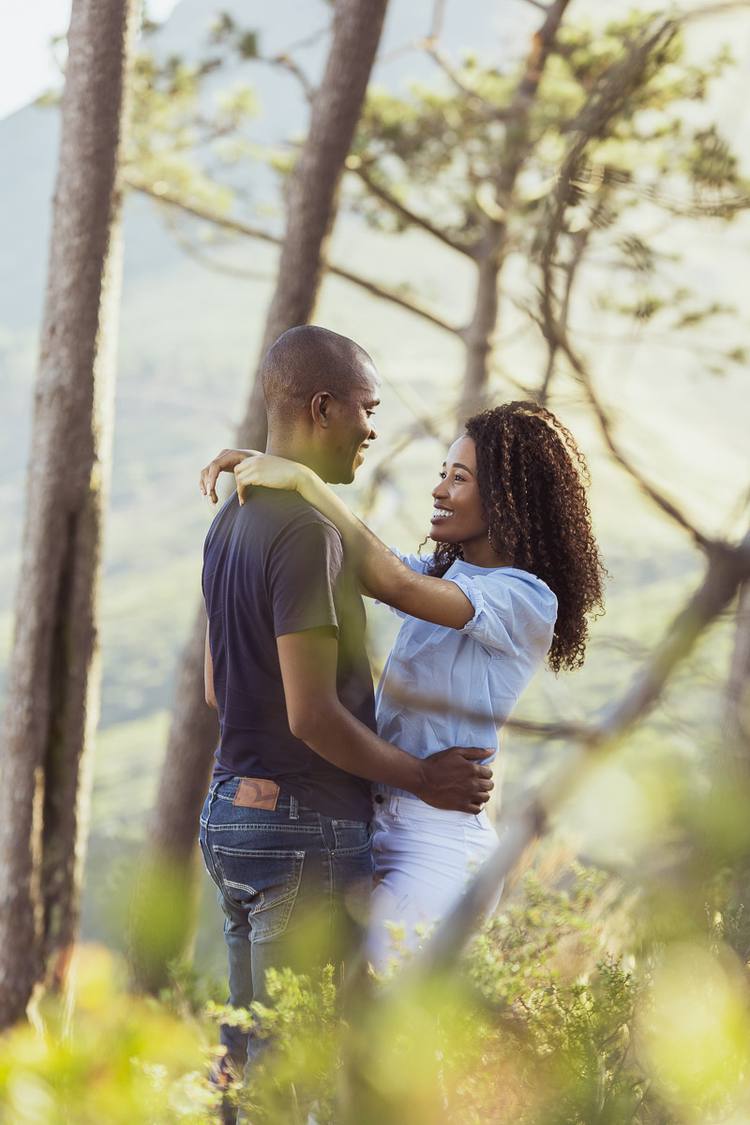 A couple embracing in a forest with sunlight filtering through the trees.