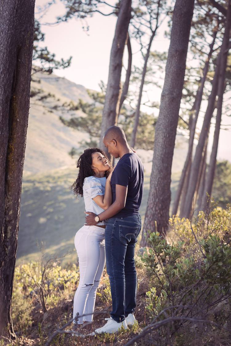 A couple embrace in a forest with a mountain in the background