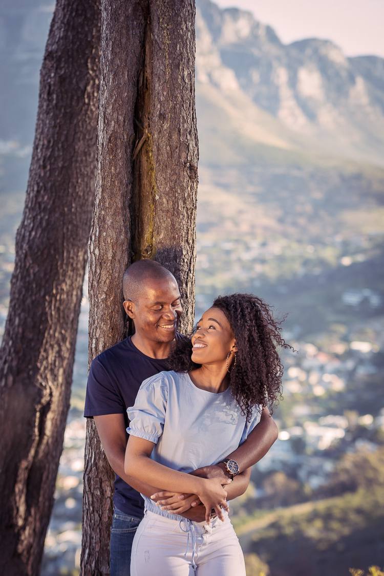 Couple smiling and embracing with a tree and mountains in the background