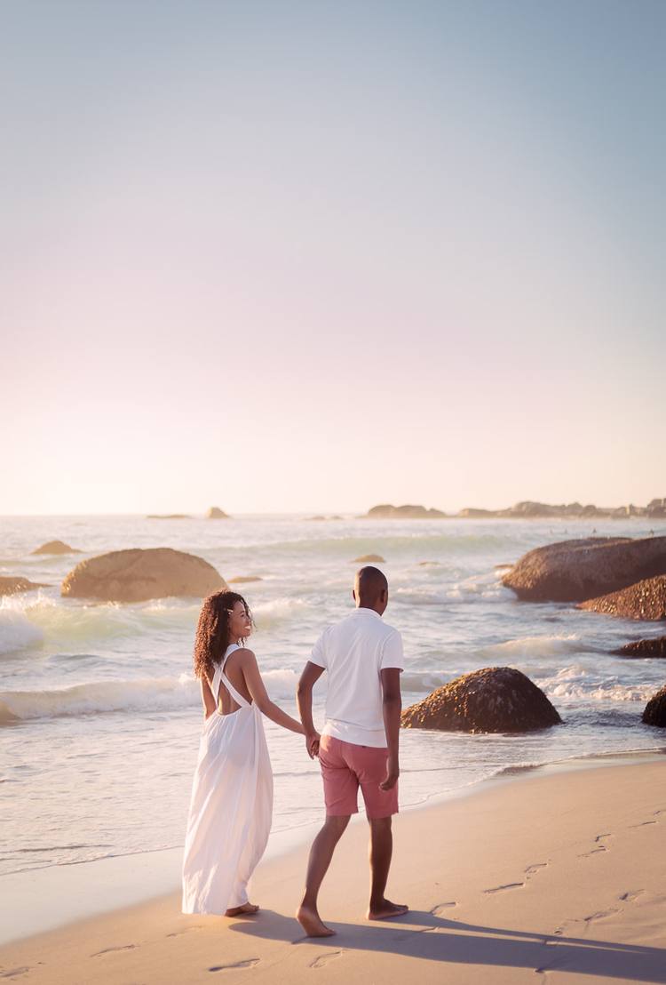 Couple walking on beach with ocean waves and rocks in background