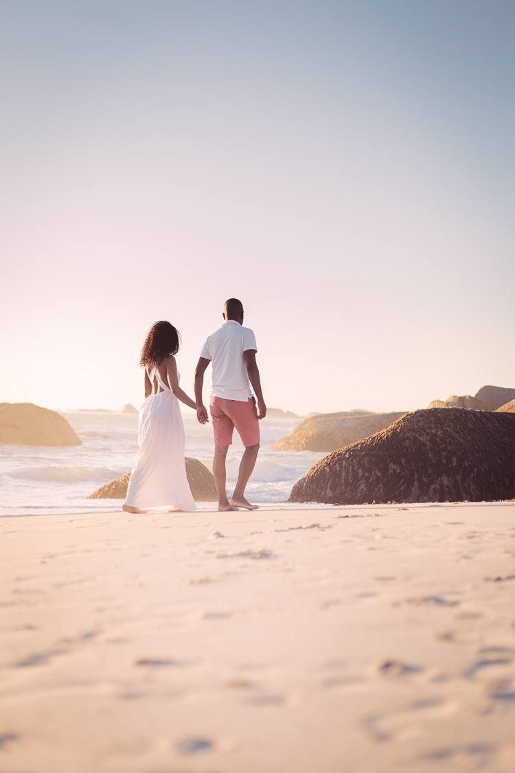 Couple walking on beach with large rocks in background