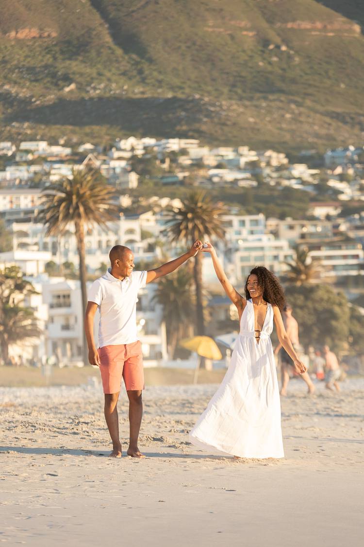 Couple dancing on beach with buildings and hills in background