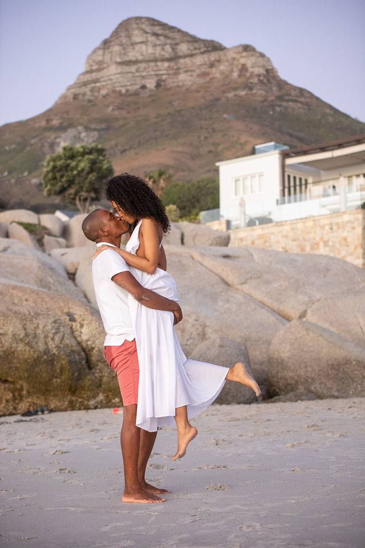Couple kissing on beach with large boulders and mountain in background
