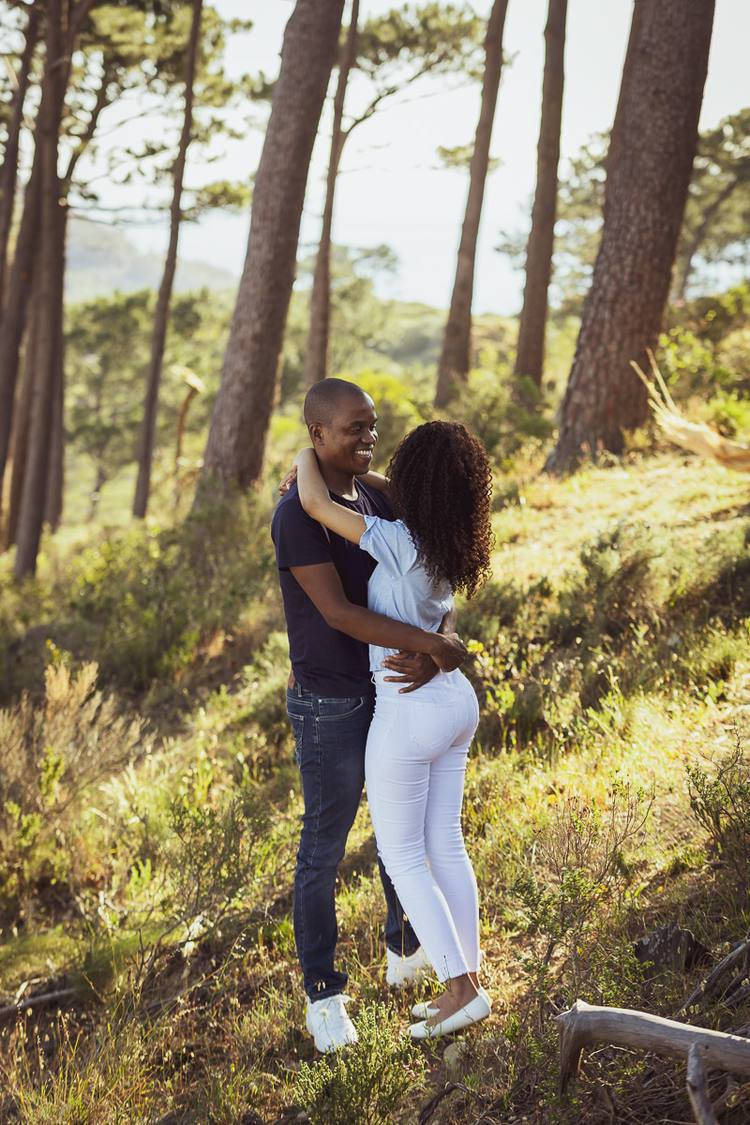 Couple embracing in a forest with tall trees and a grassy undergrowth