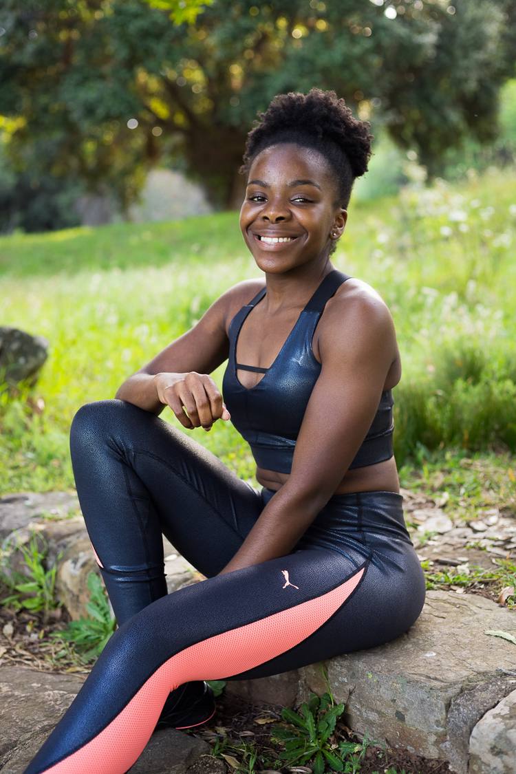 Woman in sports gear sitting on a rock in a park.