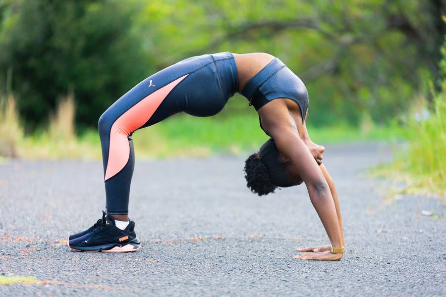 Woman in sports gear performing a back bend on a road with trees in the background