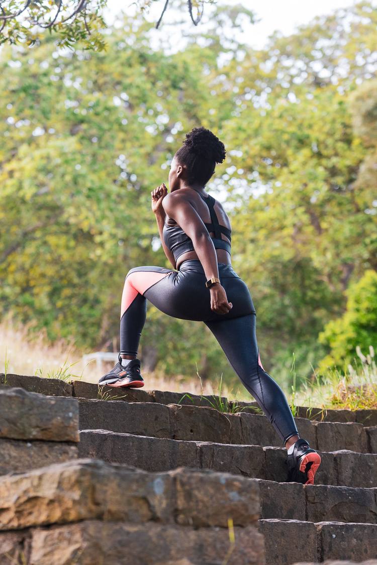Woman in sports gear climbing stone steps in a park with trees in the background