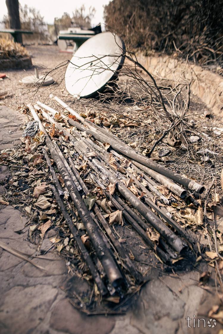Charred remains of wooden poles and a satellite dish on a stone pathway.