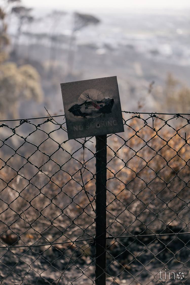 A burnt fence with a sign reading 'No Smoking