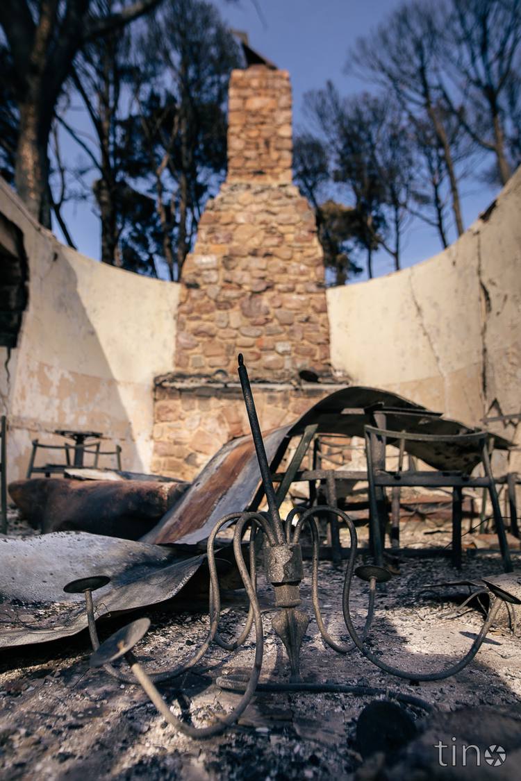 Burned remains of a lamp stand and tables in front of a stone chimney