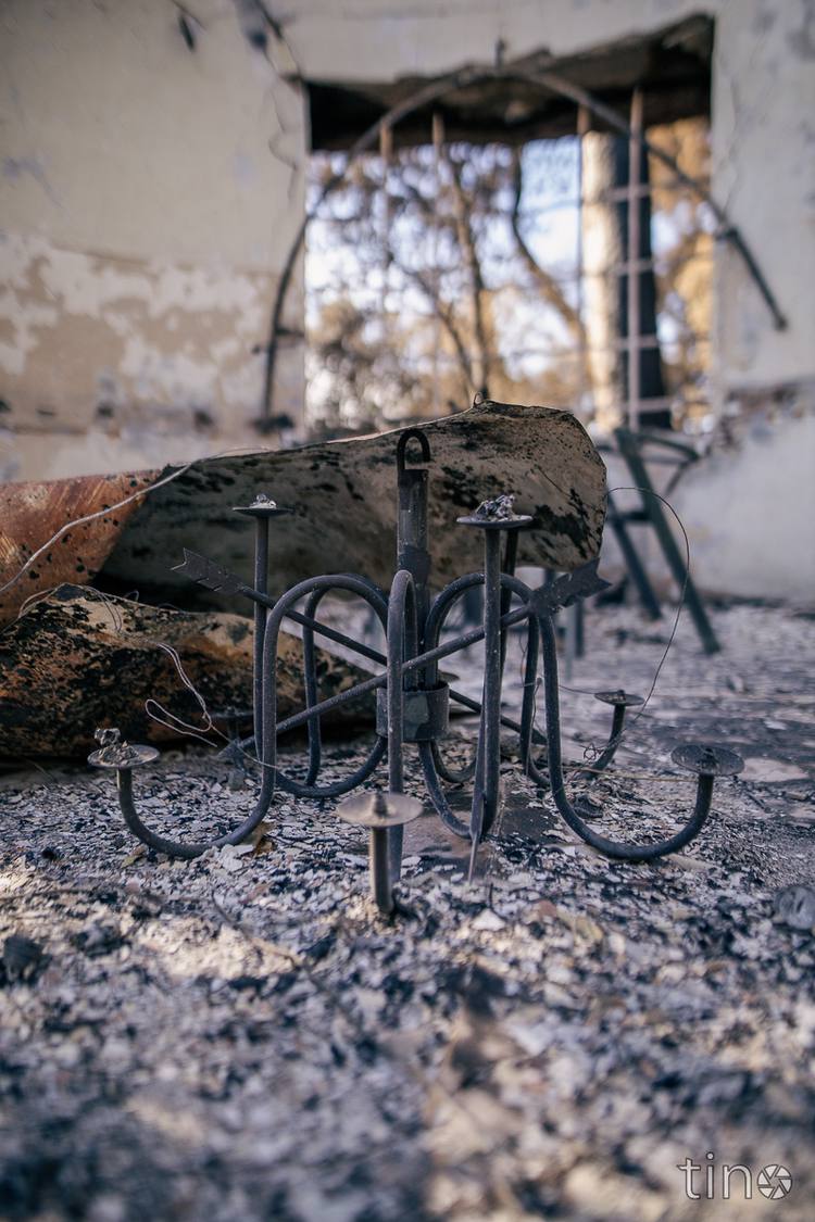 A burnt candle holder lies on the ground in front of a ruined building