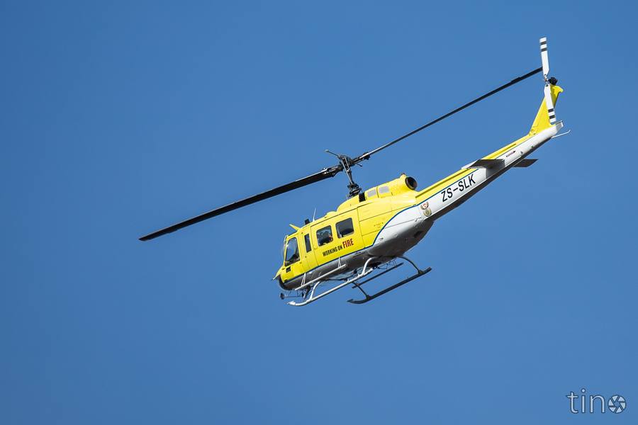 Yellow helicopter with 'Working on Fire' text flying against blue sky