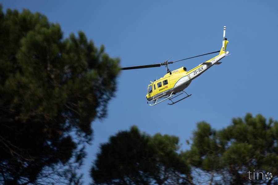 A yellow helicopter flying above trees with the text 'Working on Fire