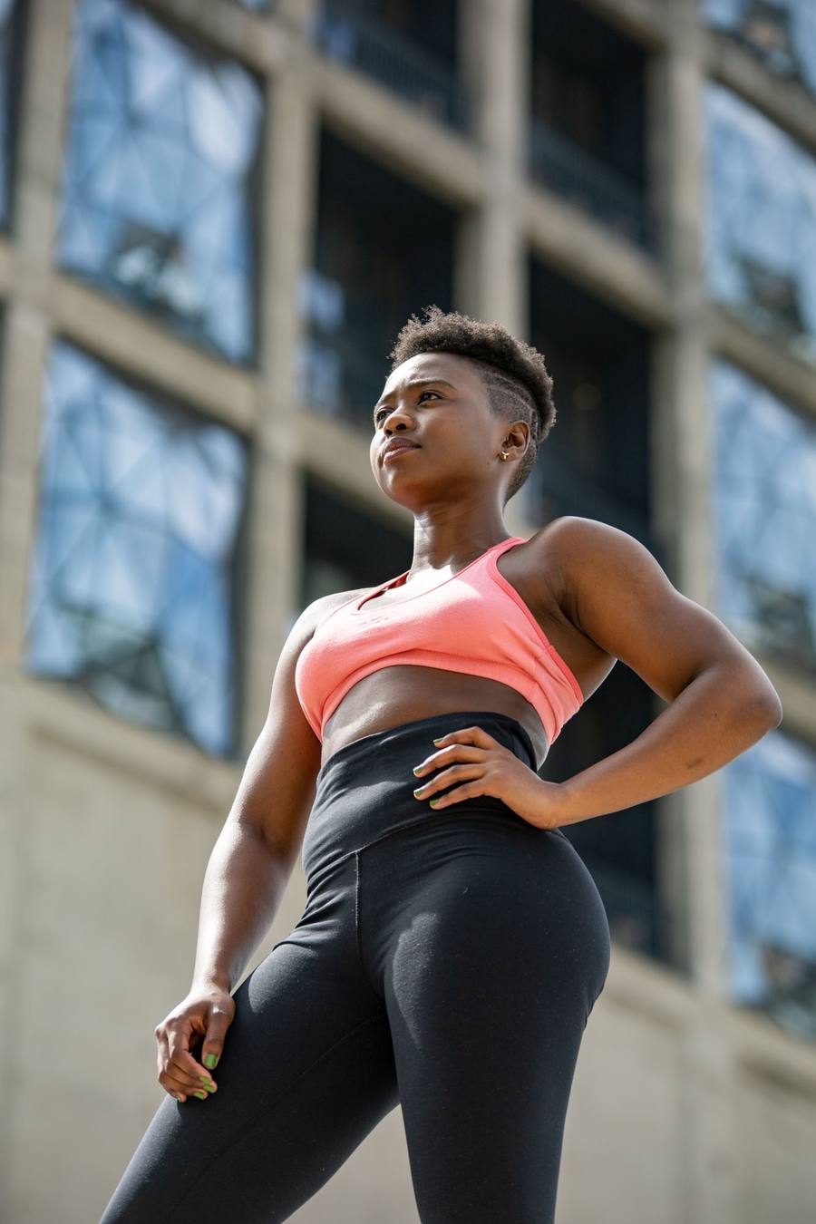 Woman in pink sports bra and black leggings standing in front of a building
