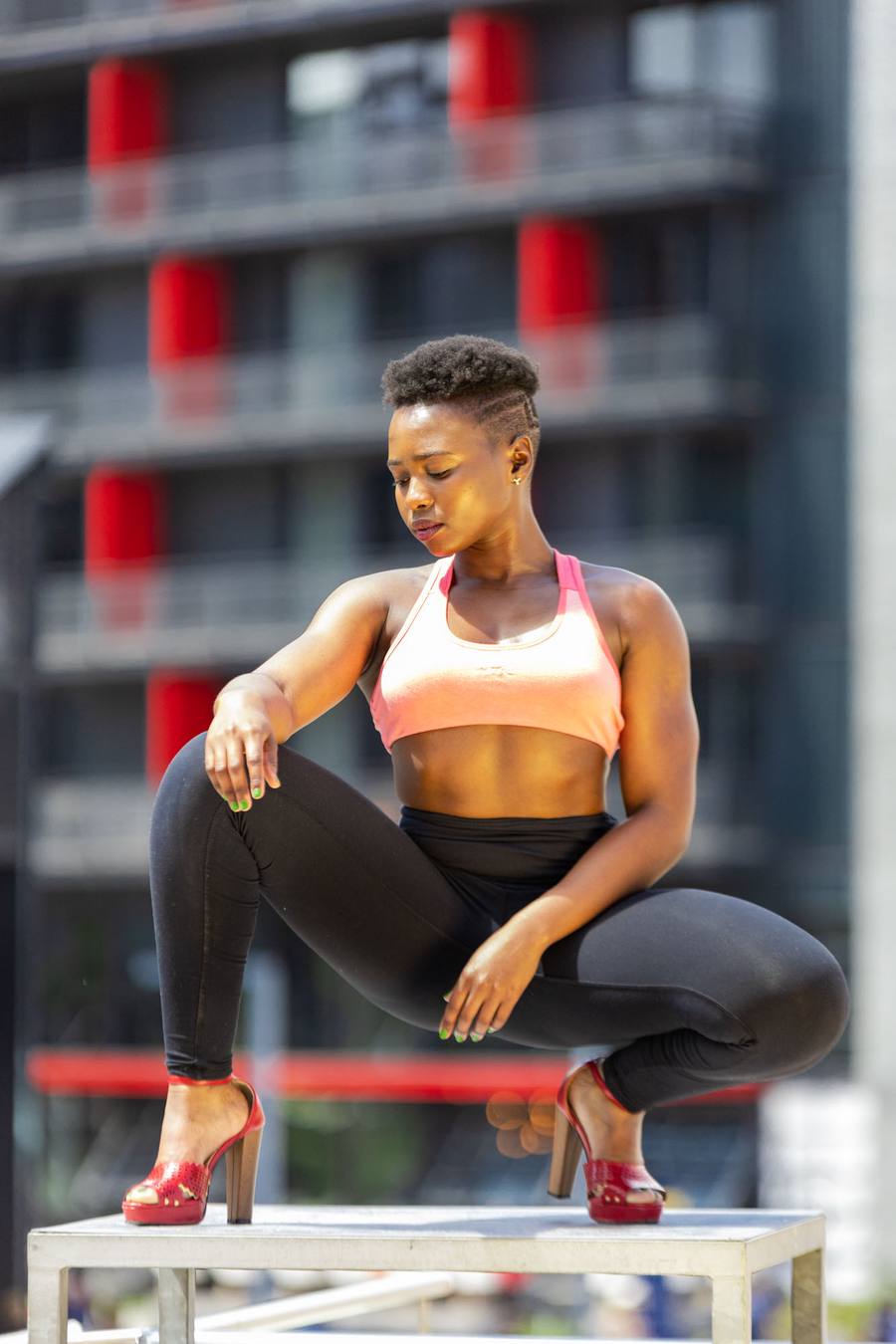 Woman in pink sports bra and black leggings doing squats on a concrete platform.