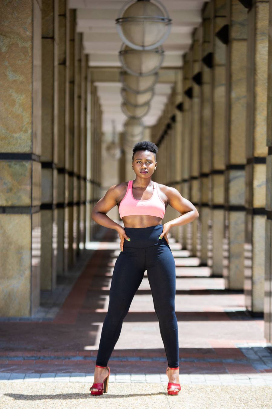 Woman in pink sports bra and black leggings posing in a corridor