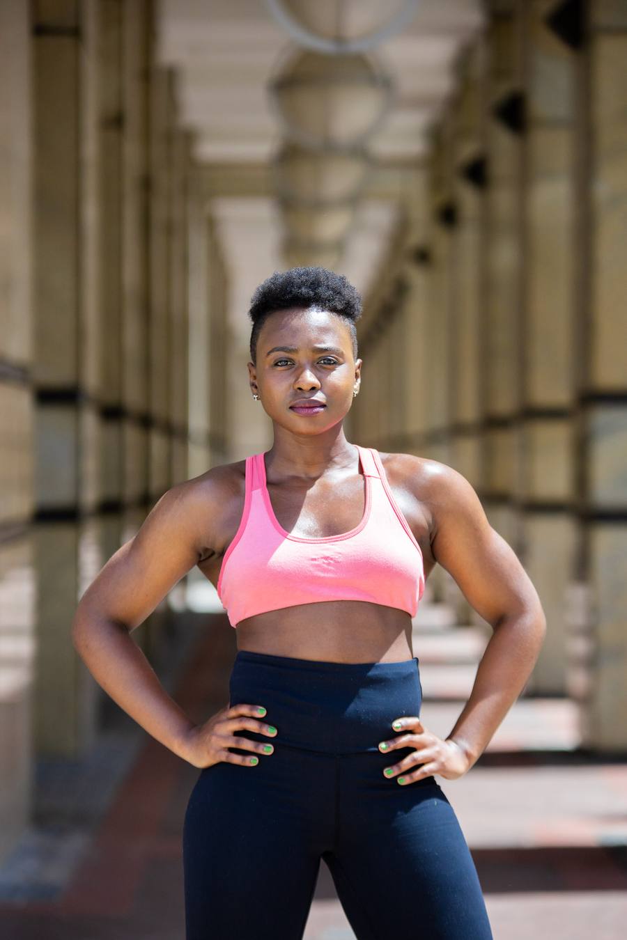 Woman in pink sports bra and blue leggings posing in a corridor