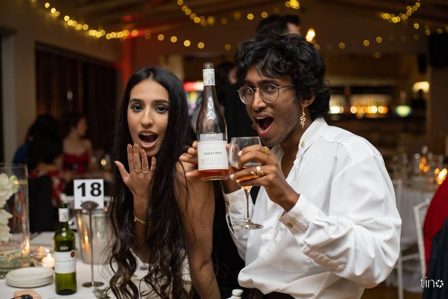 A couple toasting with wine glasses and a bottle of Shiraz Rose at a wedding reception.