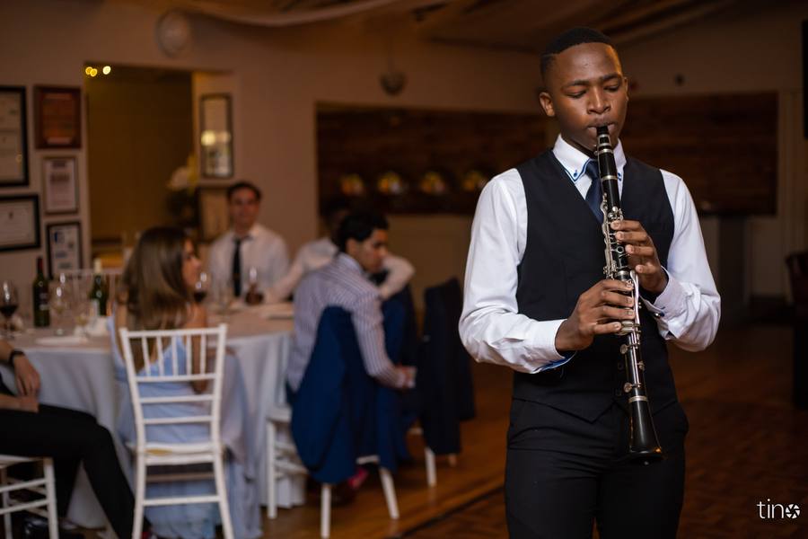 Man playing clarinet at a formal event with guests seated at tables in the background