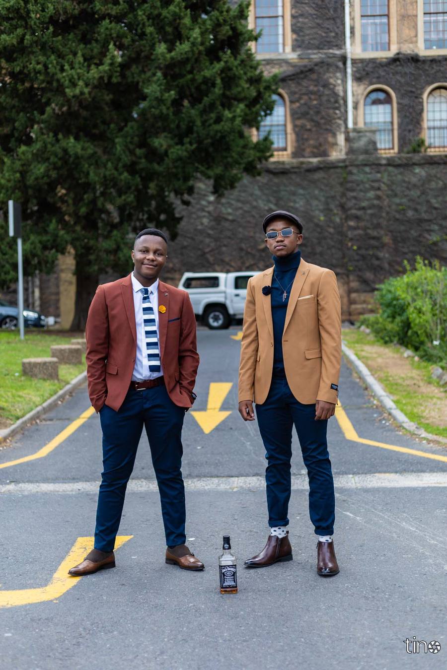 Two men in formal wear standing in a street with a bottle of Jack Daniels