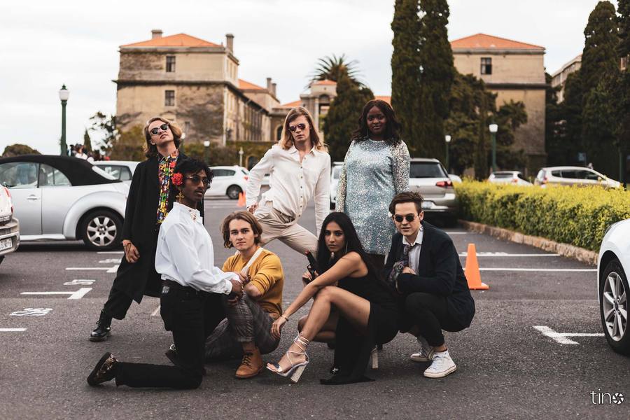 Seven people pose in a car park with buildings and cars in the background.