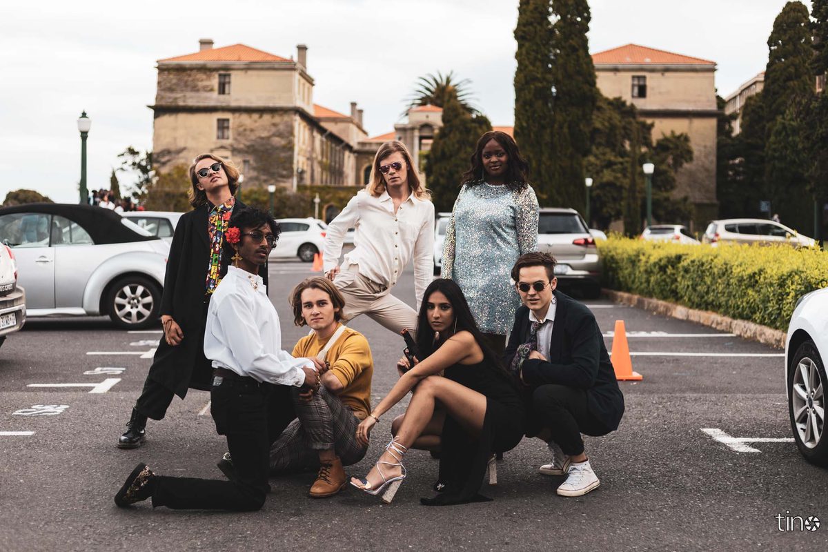 Seven people pose in a car park with buildings and cars in the background.